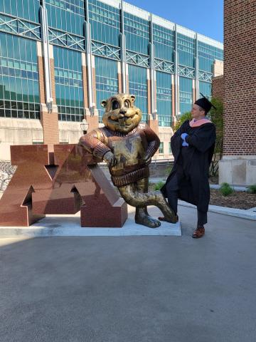 A photo of Robert Brehm in his graduation robes, standing with the Minnesota mascot. 