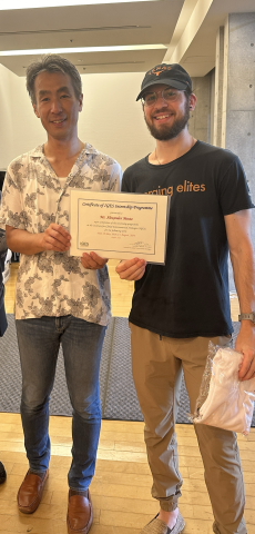 Photo of Zander standing with a man, smiling at the camera while he receives a certificate