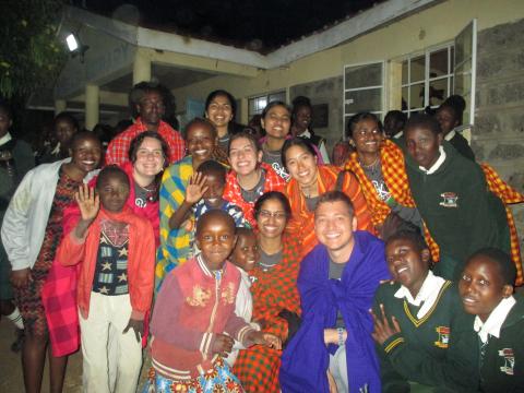 Group photo of people outside at night, all smiling and waving at the camera.