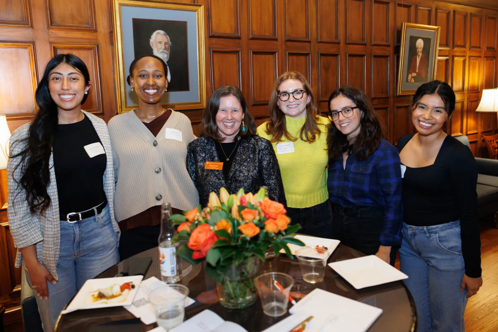 Moira Porter stands with a group of 5 students around a table at an vent reception, smiling at the camra.