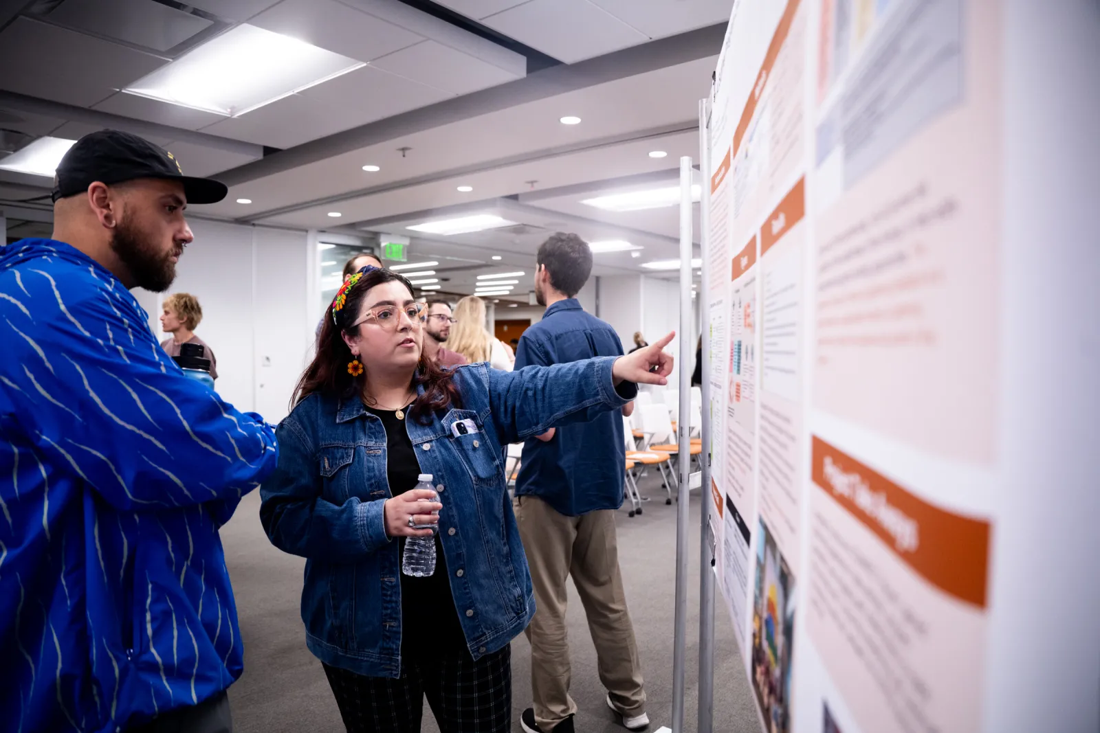 Kendra Chavera points to a research poster, talking to a fellow classmate.