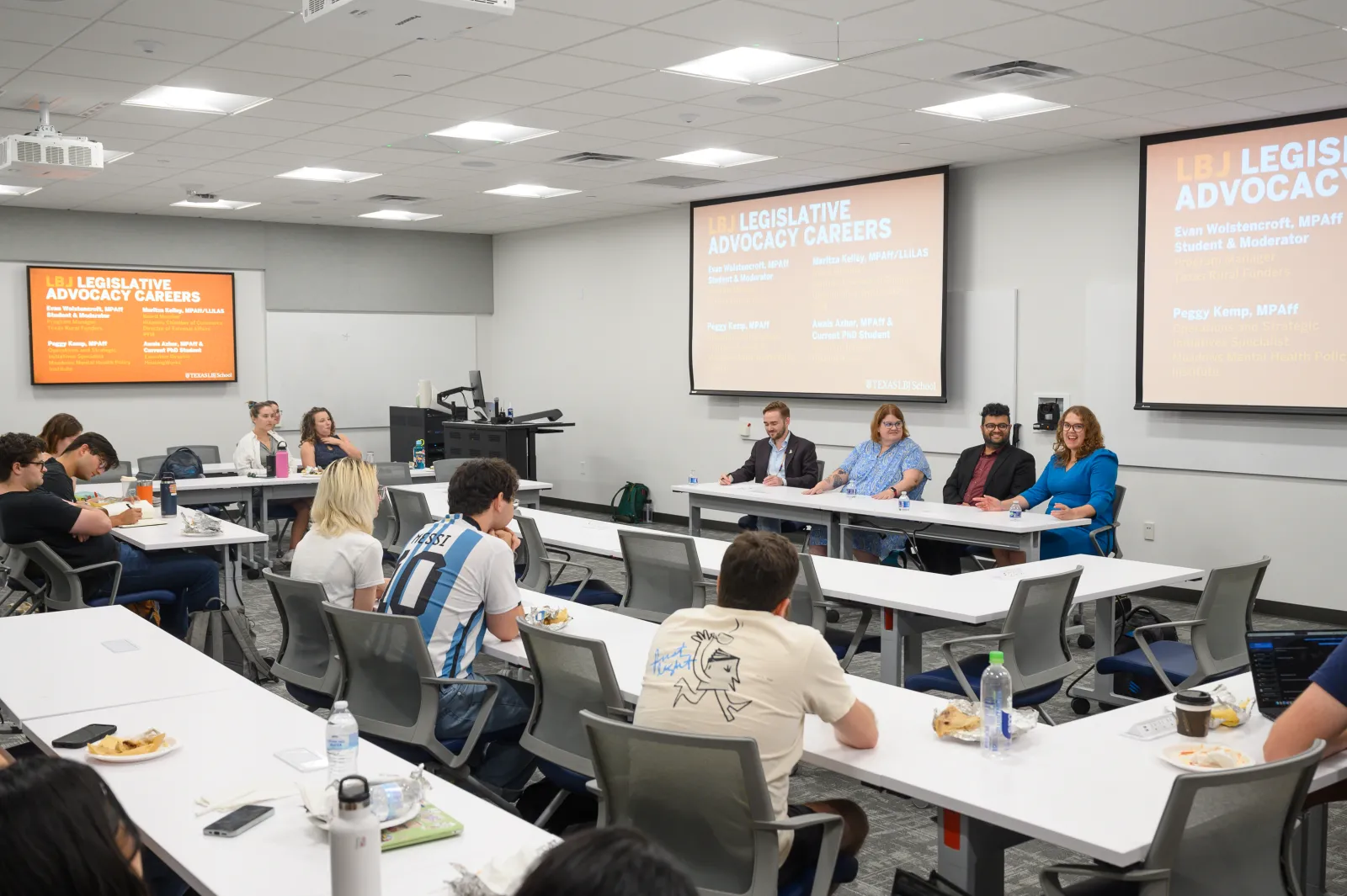 A classroom with students sitting in rows and a panel of alumni sitting at the front.