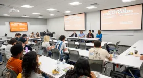 Photo of a classroom with students sittin gin rows. Three panelists and a student moderator are sitting in a row at the front of the classroom.