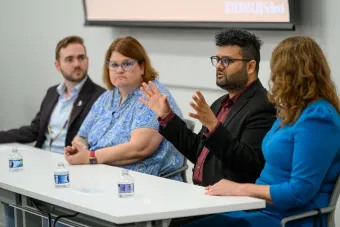 A group of three alumni and one student sitting at a table on a panel. One alumni is speaking and gesturing with his hands.