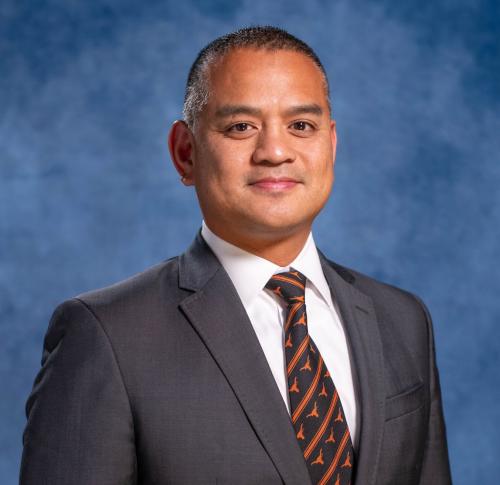 Headshot of Gerald Napoles. He has short brown hair and is wearing a suit with a tie that has UT Longhorn logos on it.
