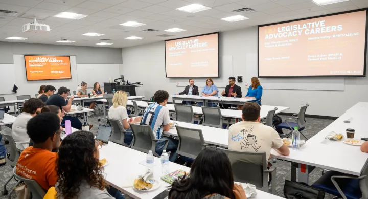Photo of a classroom with students sittin gin rows. Three panelists and a student moderator are sitting in a row at the front of the classroom.
